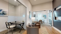 Located at 3788 Old Port Royal Rd N in Spring Hill, TN, this thoughtfully designed single-floor space offers a generous layout encompassing a living room, dining room, and a dedicated office. The interior is characterized by light hardwood flooring throughout the main areas, soaring ceilings, and a neutral color palette of crisp whites and soft grays that creates a bright, airy atmosphere.

The living room is a welcoming area filled with natural light from large windows fitted with white blinds, providing views of the surrounding neighborhood. The space accommodates comfortable seating arrangements and is accented with contemporary artwork and warm accent tones.

The private office is defined by striking floor-to-ceiling glass partition walls with frosted logo detailing, offering both visibility and privacy. The office features a sleek work desk and additional seating, making it well-suited for professional use.

The dining room is carpeted and features a round glass-top table with mid-century modern wood chairs, a wall-mounted television, and a window that allows natural light to filter in. Colorful abstract artwork adds a creative touch to the space.

A larger open area connects the dining and living zones, highlighted by bold navy ceiling beams, recessed lighting, a fireplace, and expansive floor-to-ceiling windows that draw in abundant light and outdoor views, completing this polished and functional space.