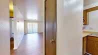 This single-floor residence offers a practical and functional layout designed for comfortable everyday living. The main living area is finished with warm hardwood-style flooring and features a ceiling fan overhead, providing a bright and airy atmosphere. A large sliding glass door dressed with vertical blinds anchors one end of the living space, allowing generous natural light to flow throughout.

The kitchen is positioned adjacent to the living area, connected via a pass-through counter that maintains an open feel between the two spaces. Warm oak-toned cabinetry lines the kitchen walls, complemented by light countertops, a stainless steel double sink, and white appliances including an electric range and refrigerator. An overhead range hood and a window above the counter add to the kitchen's practicality.

The bedrooms are carpeted in neutral tones and feature textured walls with simple, clean finishes. Each room is accessed through solid wood-toned doors and offers a calm, restful environment. The bathroom is equipped with a full-size soaking tub and shower combination, a toilet, and hardwood-style flooring, all presented in a clean, white palette. Textured ceilings throughout the unit add a classic residential character to the overall design.