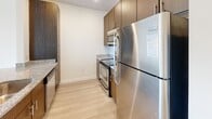 Located at 1308 Roseneath Rd in Richmond, Virginia's Scott's Addition neighborhood, this single-floor unit showcases a clean, contemporary design throughout. Light-toned wood-style flooring runs continuously across all living areas, creating a cohesive and airy feel. Crisp white walls and recessed lighting contribute to a bright, open atmosphere.

The kitchen is well-appointed with dark walnut-toned cabinetry, granite countertops, and a full suite of stainless steel appliances, including a refrigerator, range, and built-in microwave. A peninsula counter connects the kitchen to the open living and dining area, making the layout practical for everyday use.

The living area is generously proportioned and flows naturally from the kitchen, with a dedicated bedroom featuring a large window fitted with horizontal blinds that admits natural light and offers outdoor views. In-unit stacked laundry is conveniently accessible from the bedroom area.

The bathroom features a wood-grain vanity with white countertop, a large wall mirror, a medicine cabinet, and a shower with a glass enclosure. Throughout, the design emphasizes a modern, understated aesthetic with functional finishes and a clean, well-maintained presentation.