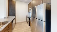 Located at 1308 Roseneath Rd in Richmond, Virginia's Scott's Addition neighborhood, this single-floor unit showcases a clean, contemporary design throughout. Light-toned wood-style flooring runs continuously across all living areas, creating a cohesive and airy feel. Crisp white walls and recessed lighting contribute to a bright, open atmosphere.

The kitchen is well-appointed with dark walnut-toned cabinetry, granite countertops, and a full suite of stainless steel appliances, including a refrigerator, range, and built-in microwave. A peninsula counter connects the kitchen to the open living and dining area, making the layout practical for everyday use.

The living area is generously proportioned and flows naturally from the kitchen, with a dedicated bedroom featuring a large window fitted with horizontal blinds that admits natural light and offers outdoor views. In-unit stacked laundry is conveniently accessible from the bedroom area.

The bathroom features a wood-grain vanity with white countertop, a large wall mirror, a medicine cabinet, and a shower with a glass enclosure. Throughout, the design emphasizes a modern, understated aesthetic with functional finishes and a clean, well-maintained presentation.