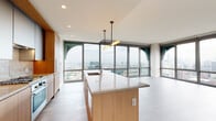 Located in Chicago's vibrant West Loop neighborhood, this contemporary high-rise unit at 164 N Peoria Street offers a sleek, modern living experience defined by clean lines and upscale finishes. The open-concept layout is anchored by a stunning kitchen featuring a large waterfall-edge island with a quartz countertop, warm natural wood cabinetry, a stone tile backsplash, and stylish pendant lighting. Floor-to-ceiling windows with distinctive arched frames wrap the living area, flooding the space with natural light and delivering expansive, panoramic views of the Chicago skyline and surrounding cityscape. The living and dining areas flow seamlessly from the kitchen, with light-toned wood-style flooring extending throughout. The bathroom is thoughtfully appointed with dual undermount sinks set into a quartz vanity, warm wood cabinetry, a wide framed mirror, and a glass-enclosed walk-in shower adorned with white square tiles and a built-in niche. Additional rooms feature the same consistent light flooring and crisp white walls, offering versatile, move-in-ready spaces. Recessed lighting throughout ensures a bright, well-lit environment. The overall ambiance is contemporary and refined, perfectly suited for urban living in one of Chicago's most sought-after neighborhoods.