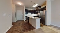 This single-floor residence at 337 Savannah Hwy in Port Royal, South Carolina, offers a well-designed open-concept layout that connects the kitchen and living areas seamlessly. The kitchen is a functional centerpiece, outfitted with dark espresso cabinetry, a white subway tile backsplash, stainless steel appliances including a refrigerator, range, microwave, and dishwasher, and a granite-topped peninsula that doubles as additional prep and casual dining space. Pendant lighting above the peninsula and a flush ceiling fixture provide layered illumination throughout the kitchen.

The living area is generously proportioned, finished with plush neutral carpeting and a ceiling fan overhead. Multiple windows allow natural light to filter in, with views of surrounding greenery, and a glass-paneled door provides direct outdoor access. Crown molding accents the living space, adding a refined architectural detail.

The bedrooms continue the warm, neutral palette with carpeted floors, ceiling fans, and windows overlooking outdoor greenery. The bathroom features dark cabinetry paired with a granite vanity top, wood-look flooring, and a shower-tub combination. Throughout the unit, the consistent use of neutral tones and quality finishes creates a cohesive and comfortable living environment.