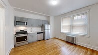 Located at 4311 Spruce St in Philadelphia's vibrant West Philadelphia neighborhood, this single-floor unit combines classic architectural character with modern updates. The open-concept main living area features warm hardwood flooring throughout, white walls, and natural light streaming in through double-pane windows fitted with blinds. A cast-iron radiator adds a charming, period-appropriate detail to the space.

The kitchen is well-appointed with gray shaker-style cabinetry extending to the ceiling for ample storage, white subway tile backsplash, light countertops, and a full suite of stainless steel appliances including a gas range, built-in microwave, dishwasher, and refrigerator. The kitchen flows seamlessly into the living area, creating an open and functional layout ideal for everyday living.

A graceful arched doorway connects the main living space to the remainder of the unit, lending a classic architectural touch. The bathroom is finished in a clean, contemporary style with dark slate-look tile flooring, a white vanity with modern hardware, and a tiled shower/tub combination with white subway tile surround. A small window provides natural ventilation. The overall aesthetic is bright, clean, and move-in ready, offering a comfortable urban living experience.