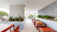 Located at 501 Broadway in Santa Monica, California, this generously sized balcony offers a well-appointed outdoor living experience in the heart of one of LA's most sought-after neighborhoods. The space features a clean, contemporary design with large-format porcelain tile flooring and a crisp white overhead canopy that provides shade while maintaining an open, airy feel.

A full-length glass railing runs along the perimeter, ensuring unobstructed views of the bustling Broadway streetscape below, the surrounding modern architecture, and the lush tree-lined sidewalks of Santa Monica. The transparency of the glass barriers enhances the sense of openness and seamlessly connects the interior to the urban environment outside.

A striking slate-gray accent wall serves as the backdrop for a raised planter box overflowing with vibrant greenery, adding a natural, garden-like element to the space. Bold orange outdoor furniture — including lounge chairs, a coffee table, and a dining set — creates a lively contrast against the neutral tones of the floor and walls, lending the balcony a warm, inviting character.

The layout is thoughtfully organized to accommodate both dining and relaxed lounging, making it a versatile outdoor retreat. Its elevated position provides commanding views of the dynamic Santa Monica streetscape and the contemporary mixed-use buildings that define this vibrant urban corridor.