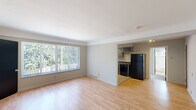 This one-bedroom, one-bathroom unit in Royal Oak, Michigan offers a practical and efficiently designed single-floor layout. The living room is a bright, open space featuring light hardwood-style flooring and a large picture window fitted with vertical blinds, allowing generous natural light and views of surrounding greenery. A bold black entry door with a small window accent provides a clean contrast to the neutral gray walls throughout. The living area flows openly toward the kitchen, which is well-appointed with gray cabinetry in an L-shaped configuration, dark countertops, a double sink, and a full suite of black appliances including a gas range, dishwasher, and refrigerator. Track lighting above illuminates the kitchen effectively. The bedroom features plush wall-to-wall carpeting, a ceiling fan with integrated lighting, a vertical-blind window, and a closet, providing a comfortable and functional retreat. The bathroom includes a full tub and shower combination with a curved curtain rod, a toilet, light wood-style flooring, and a frosted window for natural light and privacy. Neutral tones and consistent finishes throughout give the unit a cohesive, move-in-ready feel.