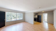 This one-bedroom, one-bathroom unit in Royal Oak, Michigan offers a practical and efficiently designed single-floor layout. The living room is a bright, open space featuring light hardwood-style flooring and a large picture window fitted with vertical blinds, allowing generous natural light and views of surrounding greenery. A bold black entry door with a small window accent provides a clean contrast to the neutral gray walls throughout. The living area flows openly toward the kitchen, which is well-appointed with gray cabinetry in an L-shaped configuration, dark countertops, a double sink, and a full suite of black appliances including a gas range, dishwasher, and refrigerator. Track lighting above illuminates the kitchen effectively. The bedroom features plush wall-to-wall carpeting, a ceiling fan with integrated lighting, a vertical-blind window, and a closet, providing a comfortable and functional retreat. The bathroom includes a full tub and shower combination with a curved curtain rod, a toilet, light wood-style flooring, and a frosted window for natural light and privacy. Neutral tones and consistent finishes throughout give the unit a cohesive, move-in-ready feel.