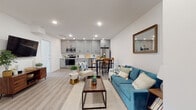This well-appointed single-floor unit showcases a thoughtfully designed open-concept layout that seamlessly connects the living, dining, and kitchen areas. Light wood-tone flooring runs throughout, complementing the bright white walls and recessed lighting that create a clean, modern atmosphere.

The kitchen is a standout feature, outfitted with sleek gray shaker-style cabinetry, white quartz countertops, and a full suite of stainless steel appliances including a range, over-the-range microwave, refrigerator, and dishwasher. A breakfast bar provides additional seating and separates the kitchen from the dining area. The open living space offers ample room for comfortable furnishings and flows naturally toward the unit's entry.

The bedrooms are bright and tranquil, each featuring large windows that invite natural light and offer views of the surrounding neighborhood. One bedroom includes a wall-mounted mini-split HVAC unit, providing individualized climate control. Both rooms feature the same wood-tone flooring found throughout the unit.

The bathrooms are finished in a contemporary style, with one featuring large-format white tile flooring and a floating vanity with a dark stone countertop and mirrored medicine cabinet, while the second bathroom offers a similarly modern aesthetic with clean lines and neutral tones throughout.