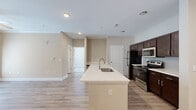 Located at 195 N Creek Dr in Summerville, SC, this single-story clubhouse showcases refined interior design with a welcoming and upscale atmosphere. The entry foyer makes an immediate impression with soaring double-height ceilings, a striking blue accent ceiling detail, decorative pendant lighting, and large-format light tile flooring. A grand arched transom window above the front door floods the entry with natural light, complemented by warm wood-accent wall paneling and an elegantly styled console.

The main lounge area is a standout, featuring exposed painted wood ceiling beams, multiple dramatic iron candelabra chandeliers, and floor-to-ceiling patterned drapery flanking expansive windows that offer views of an outdoor pool area. Rich hardwood-style flooring flows throughout, anchoring an eclectic mix of leather accent chairs, neutral upholstered seating, geometric wood cabinetry, and curated decorative accessories.

A connected lounge and seating nook offers additional gathering space, with wainscoting detail, a gallery wall of landscape artwork, and open metal shelving against a warm wood feature wall. A separate dining area with glass-top tables and upholstered chairs provides a more intimate setting. Throughout the space, layered lighting, thoughtful décor, and an open layout create a cohesive, sophisticated environment ideal for community gatherings.
