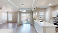 This well-designed single-floor residence offers a clean, modern aesthetic with thoughtful finishes throughout. The open-concept living and dining area serves as the heart of the home, showcasing striking herringbone-patterned flooring, crown molding, and a tray ceiling accented by a bold circular pendant light. A sliding glass door floods the space with natural light and provides direct access to an outdoor patio area with greenery views.

The kitchen is both functional and stylish, featuring white shaker cabinetry, a subway tile backsplash, stainless steel appliances including a range, microwave, and refrigerator, and a sleek white countertop peninsula with an undermount sink. Elegant cylindrical pendant lights complete the kitchen's refined look.

The bedrooms are generously proportioned, with crown molding, large windows that invite natural light, and the same herringbone flooring that flows throughout the home. A ceiling fan adds comfort to the primary bedroom space.

The bathroom area includes white cabinetry with a white countertop vanity, a wall-mounted mirror, and access to closet space, maintaining the home's clean and cohesive design language.

Neutral warm-toned walls and consistent flooring tie each room together, creating a bright, airy, and move-in-ready living environment.
