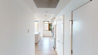 This single-floor residence showcases a clean, contemporary design defined by an open layout, light hardwood flooring, and an abundance of natural light. The kitchen is a standout feature, equipped with stainless steel appliances including a gas range, built-in microwave, dishwasher, and a French door refrigerator. Light wood cabinetry, a pale subway tile backsplash, dark countertops, and globe pendant lights suspended from a brass rail lend the space a refined, modern aesthetic. A large island with bar seating provides both workspace and casual dining. The primary bedroom is generously proportioned, featuring floor-to-ceiling wood-framed windows that frame expansive views of the waterfront and cityscape. It connects to a spacious walk-in closet with custom wood shelving and a luxurious en-suite bathroom. The primary bath is appointed with a freestanding soaking tub, a glass-enclosed walk-in shower with tile surround, warm tile flooring, and a wide vanity with a backlit mirror. A secondary bathroom mirrors the modern aesthetic with a similarly styled vanity and tile flooring. Additional highlights include in-unit laundry, generous storage, and large windows throughout that flood every room with natural light and sweeping urban and waterfront views.