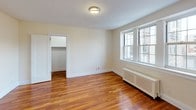 This single-floor unit offers a thoughtfully laid-out interior finished with rich, warm-toned hardwood flooring that flows consistently throughout the living spaces. The layout includes multiple rooms, each characterized by soft neutral wall tones and clean white trim that contribute to a bright, airy atmosphere.

The main living areas are generously proportioned, with large multi-pane windows that invite abundant natural light and provide views of the surrounding neighborhood. Classic radiator units beneath the windows underscore the timeless character of the space.

The bedrooms are well-sized and practical, each featuring dedicated closet space with built-in shelving for organized storage. The rooms share the same consistent hardwood flooring and neutral palette, creating a cohesive, calm environment throughout.

The bathroom presents a classic design with white square tile work covering the walls and a mosaic tile floor. A pedestal sink and a medicine cabinet mirror complete the clean, functional aesthetic, accented by a lighted vanity bar overhead.

The kitchenette area is equipped with white cabinetry offering generous storage, paired with rich granite countertops and a stainless steel sink — a practical and polished workspace. An entry door and additional closet storage round out the unit's functionality, making this a well-appointed and versatile space.