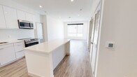 This single-floor residence showcases a clean, modern design with a bright, open-concept layout and cohesive contemporary finishes throughout. The heart of the space is the kitchen, which features a large central island with a white quartz countertop, high-gloss white cabinetry extending to the ceiling, a stone tile backsplash, and a full suite of stainless steel appliances including a refrigerator, range, dishwasher, and built-in microwave. The kitchen flows seamlessly into the open living area, which is bathed in natural light from large windows and finished with warm wood-look flooring and recessed lighting overhead. Two well-proportioned bedrooms each offer wide windows that bring in abundant natural light, wood-look flooring, ceiling fans, and sliding closet doors for ample storage. The two bathrooms are finished in a consistent modern palette, featuring white floating vanities with quartz countertops, backlit mirrors, tile flooring, and accessible grab bars. One bathroom includes a double-sink vanity and a walk-in tiled shower. Throughout the residence, crisp white walls, clean lines, and quality materials come together to create a bright, airy, and functional living environment.