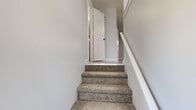 Located at 122 Peters Dr in Groton, Connecticut, this multi-level property spans three floors and offers a clean, modern aesthetic throughout. The lower level features a spacious room with durable epoxy-coated flooring, providing versatile utility space ideal for storage or a recreation area. Carpeted stairs with a white railing connect the floors, contributing to the home's cohesive design.

The main living level is anchored by a well-designed kitchen showcasing white upper cabinetry, soft grey-blue lower cabinets with matte black hardware, white quartz countertops, and a tasteful subway tile backsplash. Stainless steel appliances — including a refrigerator, electric range, dishwasher, and microwave — complete the kitchen. Light wood-look flooring runs throughout this level, and a window brings in natural light with views of the surrounding neighborhood.

The upper floors host multiple carpeted bedrooms finished in neutral grey tones, each offering generous proportions. Several rooms feature large windows overlooking a wooded natural backdrop, creating a serene atmosphere. Baseboard heating is present throughout. The bathroom is appointed with large-format grey wall tile surrounding the soaking tub, wood-look flooring, and a grey vanity, delivering a polished and functional finish.