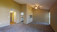 This single-floor space is defined by its vaulted ceilings in the main living area, which create a strong sense of openness and volume. A ceiling fan with a light fixture is centrally positioned, providing both airflow and ambient lighting. The living area is carpeted and features warm, neutral-toned walls throughout. A built-in wall niche adds a subtle architectural detail, while an opening leads to the adjoining kitchen. Large sliding glass doors and a side window in the living area allow ample natural light to filter in, complemented by vertical blinds for privacy.

The kitchen is efficiently laid out with white cabinetry, granite-style countertops, wood-look plank flooring, and a full suite of stainless steel appliances including a range, over-range microwave, and refrigerator. A wall-mounted thermostat is conveniently located nearby.

The bedroom continues the carpeted flooring and vaulted ceiling design, with a ceiling fan and a window that introduces natural light. A louvered closet door provides storage access.

The bathroom features wood-look flooring, a tiled tub-shower combination, a granite-topped vanity, and brushed nickel fixtures, offering a clean and functional finish throughout.