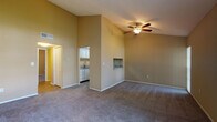 This single-floor space is defined by its vaulted ceilings in the main living area, which create a strong sense of openness and volume. A ceiling fan with a light fixture is centrally positioned, providing both airflow and ambient lighting. The living area is carpeted and features warm, neutral-toned walls throughout. A built-in wall niche adds a subtle architectural detail, while an opening leads to the adjoining kitchen. Large sliding glass doors and a side window in the living area allow ample natural light to filter in, complemented by vertical blinds for privacy.

The kitchen is efficiently laid out with white cabinetry, granite-style countertops, wood-look plank flooring, and a full suite of stainless steel appliances including a range, over-range microwave, and refrigerator. A wall-mounted thermostat is conveniently located nearby.

The bedroom continues the carpeted flooring and vaulted ceiling design, with a ceiling fan and a window that introduces natural light. A louvered closet door provides storage access.

The bathroom features wood-look flooring, a tiled tub-shower combination, a granite-topped vanity, and brushed nickel fixtures, offering a clean and functional finish throughout.