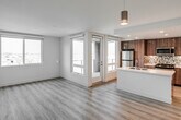 This thoughtfully designed single-floor residence at 17600 Cartwright Rd in Irvine, California offers a seamless open-concept layout that connects the living, dining, and kitchen areas into one cohesive, light-filled space. Light wood-tone flooring flows throughout, complementing the clean white walls and recessed lighting that give the interior a bright, airy character.

The kitchen is a standout feature, outfitted with rich walnut-toned cabinetry, a mosaic tile backsplash in neutral tones, stainless steel appliances including a gas range, microwave, and refrigerator, and a generous white quartz island with an undermount sink and pendant lighting above. The open layout allows the kitchen to serve as both a functional workspace and a social hub.

The living area is generously proportioned and benefits from abundant natural light streaming through large windows and glass doors that open to an outdoor space with expansive views of the surrounding Irvine cityscape. The bedroom is a calm, minimalist retreat with large windows that continue the theme of natural light and outdoor views. The bathroom features warm wood cabinetry, a white quartz dual vanity, a large wall mirror, and a full tub-shower combination, all finished with light hardwood flooring for a cohesive look.