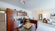 This thoughtfully designed 2-bedroom, 2-bathroom residence at 800 Aventura Way in Saint Peters, MO offers a comfortable and functional single-floor layout. The kitchen is a standout feature, showcasing rich wood cabinetry, granite-style countertops, stainless steel appliances including a range, microwave, and refrigerator, and hardwood-style flooring that adds warmth to the space. A convenient breakfast bar area with dark countertop cabinetry provides additional prep and storage space. The open living room is bathed in natural light through large sliding glass doors that lead to a private balcony with outdoor views, creating a seamless indoor-outdoor connection. Soft carpet flooring runs throughout the living and bedroom areas. Both bedrooms are well-sized and serene, each featuring carpeted floors, natural light from windows, and ample closet space with classic panel doors. The primary bathroom offers a standalone walk-in shower with glass doors and a wood-trimmed vanity, while the secondary bathroom includes a full soaking tub and shower combination. A dedicated in-unit laundry area with wire shelving and full-size washer and dryer adds everyday convenience. The overall ambiance is clean, neutral, and inviting.