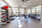 Located at 1551 Riverside Pkwy in Douglasville, Georgia, this dedicated fitness center offers a comprehensive exercise facility within a single, thoughtfully designed space. The room features a neutral gray color palette, smooth durable flooring, and white trim accents that lend a clean, modern aesthetic throughout.

Natural light pours in through multiple sets of windows positioned along the walls, including a row of upper transom-style windows that brighten the space without sacrificing wall real estate needed for equipment. Large wall-mounted mirrors on one side of the room visually expand the space and allow users to monitor their form during workouts.

Overhead, oversized ceiling fans provide consistent air circulation across the entire floor, contributing to a comfortable workout environment. Recessed lighting supplements the natural light to ensure the space is well-illuminated at all times.

The facility is equipped with an impressive range of fitness equipment, including treadmills, elliptical machines, a rowing machine, and a multi-station cable machine for strength training. A dedicated free weights area features a full rack of dumbbells alongside an adjustable workout bench. Functional training accessories such as TRX suspension trainers, kettlebells, medicine balls, and battle ropes are organized on a dedicated storage rack. A wall-mounted television and additional storage cabinetry complete this well-appointed fitness space.