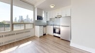 Located at 66 Spadina Rd in Toronto's sought-after Annex neighbourhood, this well-designed studio unit offers a thoughtfully utilized single-floor layout encompassing a combined living room and kitchen, plus a full bathroom. Light-toned laminate hardwood flooring runs throughout the main living area, lending a clean and cohesive aesthetic. The open-concept living space is bright and airy, benefiting from floor-to-ceiling windows that invite abundant natural light and frame views of the Toronto skyline. Built-in open shelving provides practical storage within the living area. The kitchen is efficiently arranged in an L-shaped configuration, featuring crisp white cabinetry, a subway tile backsplash, dark countertops, and a full suite of stainless steel appliances including a refrigerator, stove, dishwasher, and built-in microwave. A large window in the kitchen area further enhances the sense of openness and offers additional city views. The bathroom is finished with classic white subway tile surrounding a full soaking tub and shower, complemented by a dark-cabineted vanity with a white basin sink, chrome fixtures, and neutral floor tile — creating a clean, timeless look throughout.