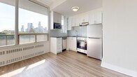 Located at 66 Spadina Rd in Toronto's sought-after Annex neighbourhood, this well-designed studio unit offers a thoughtfully utilized single-floor layout encompassing a combined living room and kitchen, plus a full bathroom. Light-toned laminate hardwood flooring runs throughout the main living area, lending a clean and cohesive aesthetic. The open-concept living space is bright and airy, benefiting from floor-to-ceiling windows that invite abundant natural light and frame views of the Toronto skyline. Built-in open shelving provides practical storage within the living area. The kitchen is efficiently arranged in an L-shaped configuration, featuring crisp white cabinetry, a subway tile backsplash, dark countertops, and a full suite of stainless steel appliances including a refrigerator, stove, dishwasher, and built-in microwave. A large window in the kitchen area further enhances the sense of openness and offers additional city views. The bathroom is finished with classic white subway tile surrounding a full soaking tub and shower, complemented by a dark-cabineted vanity with a white basin sink, chrome fixtures, and neutral floor tile — creating a clean, timeless look throughout.