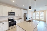 Located at 1100 Enterprise Way NW in Huntsville, Alabama, this thoughtfully designed one-bedroom, one-bathroom residence offers a clean, modern aesthetic across a single floor. The open-concept kitchen and living area serves as the heart of the home, featuring a large center island with a quartz countertop and undermount sink with a matte black faucet. White shaker-style cabinetry with black hardware lines the kitchen walls, complemented by a classic white subway tile backsplash and stainless steel appliances, including a French door refrigerator, electric range, and over-the-range microwave. Stylish pendant lights hang above the island, adding a contemporary touch. Light wood-tone flooring flows throughout, creating a bright and cohesive feel. The living area benefits from natural light through large windows with views of the surrounding neighborhood. The well-proportioned bedroom includes a ceiling fan, a large window framing outdoor views, and direct access to the bathroom. The bathroom is elegantly appointed with a single vanity featuring quartz countertops, a framed mirror, a glass-enclosed walk-in shower with white tile surround, and an adjacent walk-in closet with built-in shelving. An in-unit laundry area completes this efficiently designed home.