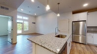 This well-appointed single-floor residence offers a thoughtfully designed open-concept layout that seamlessly connects the kitchen, dining, and living areas. The kitchen serves as a central hub, anchored by a large island with granite countertops, an undermount sink, and stylish pendant lighting. White shaker cabinetry provides ample storage, while a full suite of stainless steel appliances — including a refrigerator, range, and over-the-range microwave — delivers a polished, modern finish. A tile backsplash adds a refined touch throughout the cooking space. In-unit washer and dryer connections are conveniently accessible just off the kitchen area. The living area is bathed in natural light, featuring soaring ceilings, transom windows, and French doors that open onto a private balcony, creating an airy, open feel. Durable hardwood-style flooring extends throughout the space, lending warmth and continuity. The bedroom offers a spacious walk-in closet and connects to the main living area through clean, open sightlines. The bathroom is finished with a full soaking tub and tiled surround. Additional windows in the secondary bedroom provide pleasant outdoor views, completing this bright and functional residence.