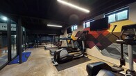 The reNew Fitness Center at 6723 Schroeder Rd in Madison, Wisconsin is a fully equipped, single-floor fitness facility designed to support a wide range of workout routines. The space is defined by its industrial-modern aesthetic, featuring a bold black ceiling with exposed structural elements and sleek linear LED lighting that creates a focused, energetic atmosphere throughout.

The main fitness floor is generously sized and houses a strong lineup of Life Fitness cardio equipment, including ellipticals, treadmills, and a rowing machine, arranged for comfortable use. A striking geometric accent wall in deep reds, yellows, and grays serves as a visual centerpiece, complemented by wall-mounted televisions for entertainment during workouts. Strength training is well-represented with a dedicated rack area stocked with free weights, medicine balls, and resistance equipment.

A separate boxing area features a heavy bag suspended from the ceiling and rubber mat flooring, enclosed by black-framed glass partitions that provide visual separation while maintaining an open feel. The entrance corridor is welcoming, with signage greeting visitors and clear sightlines into the main workout space.

The facility also includes a practical laundry room equipped with commercial washers and dryers, accented by deep blue walls. Natural light filters in through ground-level windows, adding brightness to the workout areas. The overall design balances functionality with a modern, motivating environment.