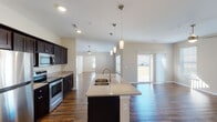 This single-story home offers a thoughtfully designed open-concept floor plan that seamlessly connects the kitchen, dining, and living areas. The kitchen is a standout feature, equipped with dark espresso cabinetry, granite countertops, stainless steel appliances—including a refrigerator, range, and built-in microwave—and a large central island with a undermount sink illuminated by stylish pendant lighting. Rich, dark hardwood-style flooring flows throughout the main living areas, complementing the neutral warm-toned walls.

The living area is bright and airy, benefiting from abundant natural light through multiple windows with blinds and a sliding glass door that opens to the backyard. A ceiling fan adds comfort to this generous space. The bedrooms continue the warm aesthetic, with ceiling fans, natural light from windows, and a mix of hardwood-style flooring and plush carpeting.

Two bathrooms serve the home, each featuring dark cabinetry with granite vanity tops. One bathroom includes a tub-shower combination and is conveniently paired with an in-unit laundry area. The other bathroom offers a walk-in shower. Completing the home is a spacious attached two-car garage with a garage door opener and concrete flooring, providing ample storage and parking.