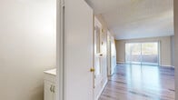 This two-floor residence offers a well-organized and functional layout with a clean, neutral aesthetic throughout. The main living area is bright and open, featuring light hardwood-style flooring that reflects natural light streaming in through sliding glass doors fitted with vertical blinds. A ceiling fan adds a practical touch to the spacious living room, which connects seamlessly to the kitchen. The kitchen is thoughtfully appointed with white cabinetry, light quartz-style countertops, a mosaic tile backsplash, stainless steel appliances including a range and dishwasher, and a double-basin sink beneath a window. A hallway lined with louvered bi-fold closet doors and a textured ceiling leads to the sleeping areas, which feature plush carpeting and large windows with horizontal blinds that frame outdoor views of surrounding greenery. The bathroom includes a white vanity with ample drawer and cabinet storage, a lighted mirror, and a full soaking tub with a clean surround, all set on wood-style flooring. Sliding glass doors in multiple rooms provide access to outdoor spaces and allow generous natural light to fill the interiors, contributing to the home's airy and well-lit ambiance throughout both levels.