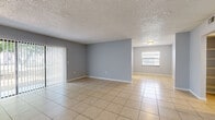 Located at 5200 64th Circle East in Saint Petersburg, Florida, this single-story home offers a practical and comfortable layout with consistent light-toned tile flooring throughout. The open living area is bright and spacious, featuring sliding glass doors fitted with vertical blinds that fill the room with natural light and provide access to the outdoors. A secondary window in the adjoining area further enhances the sense of openness. The kitchen is efficiently designed with white cabinetry, light stone-look countertops, a subway tile backsplash, a double stainless steel sink, and a window overlooking the greenery outside. The bedrooms are generously sized, each finished with the same neutral tile flooring, soft gray walls, and sliding closet doors providing ample storage. One bedroom features a walk-in style closet, while another includes a dedicated laundry area. The bathroom is neatly appointed with mosaic tile flooring, a granite-topped vanity with white cabinetry, and a full tub-shower combination with a window for natural ventilation. Textured ceilings are present throughout the home, and the overall color palette of soft gray and white lends a clean, neutral aesthetic throughout this Saint Petersburg residence.