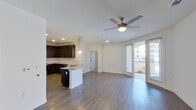 This single-floor unit offers a thoughtfully designed open-concept layout where the kitchen and living area flow seamlessly together. The kitchen is a standout feature, equipped with dark espresso cabinetry extending to the ceiling, granite countertops, a stainless steel appliance suite including a range, over-the-range microwave, refrigerator, and dishwasher, and a central island with a stainless steel sink. Elegant teardrop pendant lights illuminate the workspace, complementing the recessed lighting throughout. Wood-look flooring runs through the main living areas, while plush carpet is found in the bedroom. The living area is anchored by a ceiling fan and opens to a private balcony through floor-to-ceiling sliding glass doors, allowing abundant natural light and outdoor views. The entryway is clean and functional, featuring wood-look flooring and a closet. The bathroom includes granite countertops, dark cabinetry, a tub-shower combination with marble-style tile surround, and direct access to a spacious walk-in closet with built-in shelving. The bedroom offers a ceiling fan, a window with an exterior view, and ample room.