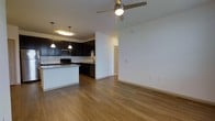 This single-story residence offers three bedrooms and two bathrooms within a thoughtfully designed open-concept floor plan. The living and kitchen areas flow seamlessly together, creating a spacious, connected environment well-suited for both daily living and entertaining.

The kitchen is a standout feature, outfitted with dark espresso cabinetry that provides a striking contrast against light-toned walls. Granite countertops add a polished, durable surface, while a kitchen island extends the prep and gathering space. Stainless steel appliances, including a built-in microwave and dishwasher, complement the modern aesthetic. Pendant lighting above the island enhances both function and visual appeal.

The open living area is finished with warm-toned hardwood-style flooring that runs throughout, contributing to a cohesive and inviting ambiance. A ceiling fan with integrated lighting provides comfort and circulation. Clean white walls and neutral tones keep the space feeling bright and versatile.

A hallway visible from the main living area leads to the bedrooms and additional rooms, suggesting a practical layout that separates living and sleeping spaces. Overall, the residence presents a modern, well-appointed interior with consistent finishes throughout.