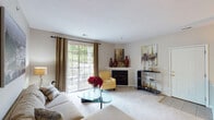 This single-floor residence offers a thoughtfully designed layout with a seamless flow between its living, dining, and private spaces. The living room serves as the heart of the home, centered around a fireplace framed by decorative accents and flanked by a stylish bar unit. Large sliding glass doors flood the room with natural light and provide direct access to a private balcony overlooking lush greenery. A columned entryway transitions gracefully into the dining area, which features warm pendant lighting and an elegant sunburst mirror, creating an inviting atmosphere for gatherings. The galley-style kitchen is efficiently arranged with white cabinetry, gold hardware, light countertops, and full appliances including a range, microwave, and refrigerator, with tile flooring throughout. The primary bedroom is a serene retreat with plush carpeting, a large window with curtains, and ample dresser space. A secondary bedroom offers comfortable proportions with bright natural light and carpeted floors. Two bathrooms serve the residence, one featuring a walk-in shower and the other a vanity with white cabinetry and tile flooring. A dedicated laundry room with a full-size washer and dryer and overhead shelving adds everyday convenience to this well-rounded home.