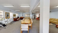 Located at 2500 Honolulu Ave in Montrose, California, this single-floor community space offers a generous and versatile layout designed to accommodate a wide range of activities. The interior is finished with soft blue walls, neutral carpet flooring, and flush-mounted fluorescent lighting throughout, creating a bright and welcoming atmosphere.

The main open area serves multiple functions, anchored by a tiled fireplace with a TV above it, providing a comfortable gathering focal point. Nearby, a dining area features a long wooden table with ample seating, suitable for group meals or meetings. A dedicated fitness corner houses several cardio machines, including stationary bikes and an elliptical trainer, with windows allowing in natural light.

A well-stocked library nook lines one wall with floor-to-ceiling bookshelves filled with a large collection of books, accompanied by comfortable armchairs ideal for quiet reading. Additional lounge seating areas are distributed throughout the space, offering cozy spots for socializing. A piano adds a cultural touch near the main gathering area.

The kitchen is equipped with wood-trimmed cabinetry, white countertops, and a double stainless steel sink, providing functional support for events and daily use. Structural columns punctuate the open floor plan, contributing to the architectural character of the space. Access to an outdoor area is available through glass doors, enhancing the connection to the surrounding environment.
