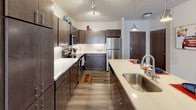 Located on Highland Drive in Menomonee Falls, Wisconsin, this single-floor residence offers a thoughtfully designed layout with modern finishes throughout. The kitchen is a standout feature, showcasing rich dark cabinetry, white quartz countertops, a subway tile backsplash, and a full suite of stainless steel appliances including a refrigerator, range, and built-in microwave. A large center island with an undermount sink and pendant lighting adds both functionality and style, while track lighting and wood-look plank flooring complete the contemporary aesthetic. The open living area is bright and welcoming, highlighted by a sliding glass door that floods the space with natural light and leads to a private outdoor patio. The bedroom is generously sized, featuring plush carpet, a ceiling fan, and a walk-in closet offering ample storage. A window provides additional natural light, enhancing the room's airy feel. The bathroom continues the home's cohesive design with dark cabinetry, a long white vanity countertop, a wide mirror, and wood-look flooring. Consistent use of dark wood tones, neutral walls, and quality finishes throughout the residence creates a modern, comfortable living environment.