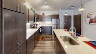 Located on Highland Drive in Menomonee Falls, Wisconsin, this single-floor residence offers a thoughtfully designed layout with modern finishes throughout. The kitchen is a standout feature, showcasing rich dark cabinetry, white quartz countertops, a subway tile backsplash, and a full suite of stainless steel appliances including a refrigerator, range, and built-in microwave. A large center island with an undermount sink and pendant lighting adds both functionality and style, while track lighting and wood-look plank flooring complete the contemporary aesthetic. The open living area is bright and welcoming, highlighted by a sliding glass door that floods the space with natural light and leads to a private outdoor patio. The bedroom is generously sized, featuring plush carpet, a ceiling fan, and a walk-in closet offering ample storage. A window provides additional natural light, enhancing the room's airy feel. The bathroom continues the home's cohesive design with dark cabinetry, a long white vanity countertop, a wide mirror, and wood-look flooring. Consistent use of dark wood tones, neutral walls, and quality finishes throughout the residence creates a modern, comfortable living environment.