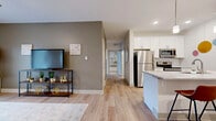 Located at 6386 Transit Rd in Lancaster, NY, this single-floor unit offers a thoughtfully designed open-concept layout with modern finishes throughout. Light-toned luxury vinyl plank flooring flows seamlessly across the main living areas, complementing the neutral color palette of warm gray and crisp white tones.

The kitchen is a standout feature, outfitted with white shaker-style cabinetry, granite-look countertops, a subway tile backsplash, and a full suite of stainless steel appliances including a refrigerator, range, microwave, and dishwasher. A peninsula with pendant lighting and bar seating connects the kitchen to the living area, making it ideal for entertaining.

The living room is bright and airy, benefiting from large sliding glass doors that invite natural light and provide outdoor views. A welcoming entryway leads directly into the combined living and dining area.

The bedrooms are comfortably sized, each featuring large windows with outdoor views and plush carpeting. The bathroom is well-appointed with white cabinetry, granite-look counters, a walk-in shower with glass doors, and consistent finishes that echo the rest of the unit. Recessed lighting throughout enhances the clean, contemporary ambiance.
