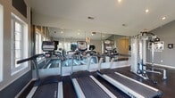Located at 55 Eastpointe Ridge Dr in Columbus, Ohio, this dedicated fitness center offers a well-equipped, single-floor workout facility designed to support a comprehensive exercise routine. The space is defined by its striking vaulted ceilings that rise to a prominent peak, creating an open and airy atmosphere throughout. A generous bank of multi-pane windows lines one wall, flooding the interior with natural light and providing views of the surrounding community.

The fitness center is outfitted with a full lineup of TRUE-brand cardio equipment, including multiple treadmills and an elliptical trainer, all arranged along a wall of floor-to-ceiling mirrors that enhance the sense of space. A recumbent bike and additional cardio options round out the aerobic training area. For strength training, the facility features a multi-station cable machine paired with a dedicated bench, as well as a tiered dumbbell rack stocked with a complete range of free weights. Dark rubber flooring throughout provides durability and comfort underfoot.

The neutral gray walls and recessed lighting contribute to a clean, modern aesthetic. An entry area with glass-paneled doors offers easy access, while additional doors provide connectivity to restroom facilities. The overall ambiance is functional, well-maintained, and inviting for residents seeking a convenient on-site fitness option.