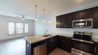 Located at 830 Porter Rd in Nashville's vibrant East Nashville community, this single-floor unit offers a thoughtfully designed open layout with contemporary finishes throughout. The kitchen serves as a central highlight, boasting dark espresso cabinetry extending to the ceiling, granite countertops, a classic white subway tile backsplash, and a full suite of stainless steel appliances including a refrigerator, electric range, built-in microwave, and dishwasher. A peninsula with an undermount sink and pendant lighting overhead creates a natural transition into the open living area, which features warm wood-tone flooring that continues throughout the unit. The living space is bright and airy, with multiple windows allowing generous natural light and a ceiling fan providing added comfort. A dedicated hallway leads to additional rooms, including closeted spaces accessed through clean white panel doors. The bathroom features a full tub-shower combination with brushed nickel fixtures and a clean, all-white surround. The overall design aesthetic is modern and understated, with neutral walls, crisp trim work, and consistent flooring creating a cohesive and move-in-ready environment well-suited to urban Nashville living.