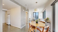 This contemporary 3-bedroom, 2-bathroom residence is designed with a clean, minimalist aesthetic across a single floor. Polished concrete floors run throughout, lending a sleek, cohesive look to every room. The open-plan living and dining area is a standout, anchored by expansive floor-to-ceiling windows with black metal frames that frame sweeping urban skyline views and flood the space with natural light. A sliding glass door in the dining area opens to an exterior balcony, further connecting the interior to the cityscape beyond.

The galley-style kitchen is efficiently laid out with white cabinetry, white appliances, light countertops, and subtle LED cove lighting along the upper cabinets, creating a bright and functional cooking space. The hallways connect the living areas to three well-proportioned bedrooms, each featuring concrete floors, clean white walls, and ceiling fans. The primary bedroom benefits from a large window with city views. The two bathrooms are finished with neutral tones, including a full tub-shower combination adorned with classic white subway tile. The overall ambiance is bright, airy, and modern, offering a refined urban living experience.