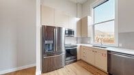 Located at 1106 Washington Ave in Golden, Colorado, this two-bedroom, one-bathroom unit offers a thoughtfully designed single-floor layout with a blend of modern updates and classic character. The kitchen is outfitted with stainless steel appliances — including a French door refrigerator, electric range, and built-in microwave — complemented by flat-panel cabinetry in a warm neutral tone, white tile backsplash, and a window that brings in natural light with views of the surrounding area. Light-toned hardwood flooring runs throughout the main living areas, lending warmth and continuity. A long, well-lit hallway with recessed lighting and textured walls connects the rooms efficiently. Both bedrooms feature plush carpeting and clean white walls; a standout design element is the exposed red brick accent wall that adds industrial character to the space. The primary bedroom also features a ceiling fan. The bathroom is finished with large-format gray tile, a glass-enclosed shower, a floating wood-toned vanity with an undermount sink, and a framed mirror. Two closets and a dedicated laundry area provide practical storage and convenience. The unit presents a cohesive aesthetic — contemporary finishes paired with raw architectural details — making it a distinctive offering in the heart of Golden.