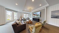 Located at 3220 Hatchet Bay Dr in Charleston, SC, this single-floor community clubhouse is thoughtfully designed to blend coastal charm with modern comfort. The interior features shiplap-paneled white walls, tray ceilings with crown molding, and recessed lighting complemented by a statement sputnik-style chandelier, all contributing to a bright and welcoming ambiance.

The expansive main lounge area is anchored by multiple seating arrangements, including a tufted leather sofa, curved sectionals, and upholstered accent chairs grouped around rustic wooden side tables. Large windows dressed with chevron-patterned valances line the walls, flooding the space with abundant natural light and offering views of the surrounding greenery. A large flat-screen television mounted above a dark credenza serves as the media focal point of the room.

A dedicated business center is seamlessly integrated into the open floor plan, featuring a long wooden work surface fitted with multiple desktop computers and ergonomic rolling chairs, accented by soft wall sconces. The transition between the lounge and business areas is defined by architectural columns and recessed wall niches, providing a sense of distinct zones while maintaining an open, cohesive flow throughout the space.