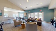 Located at 234 McMillan Ct in Cortland, Illinois, this single-story community clubhouse is thoughtfully designed to foster comfort, socializing, and everyday convenience. The main lounge area is a standout feature, boasting vaulted ceilings, recessed lighting, and bold teal accent walls that create a vibrant yet relaxed atmosphere. Generous seating — including a large sectional sofa, accent chairs, and a sleek coffee table — provides ample space for gatherings of all sizes. Multiple sets of French doors flood the lounge with natural light while offering direct views of the surrounding outdoor areas. Adjacent to the lounge, a dedicated dining zone features a dark-wood table with upholstered chairs, accented by a striking piece of wall art, and benefits from additional natural light through large windows with views of the outdoor pool area. The kitchen is well-appointed with warm wood cabinetry, a mosaic tile backsplash, a full-size refrigerator, and a peninsula with counter seating — ideal for catering or casual use. Neutral carpet throughout the lounge and dining areas adds warmth underfoot, while tile flooring in the kitchen ensures easy maintenance. The overall design balances practicality with an inviting aesthetic, making this clubhouse a functional and welcoming hub for the community.