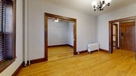 This one-bedroom, one-bathroom unit at 225 W 15th St in Minneapolis, MN offers a compact yet characterful living space defined by classic architectural details. Rich, dark-stained wood trim frames the doorways, windows, and baseboards throughout, lending a warm, traditional aesthetic that pairs beautifully with the light-toned hardwood floors found across the living and bedroom areas. The living room is a bright, open space anchored by an elegant chandelier and natural light streaming through double windows with classic wood surrounds. A cast-iron radiator adds to the vintage charm while providing reliable heat. The bedroom is an intimate, cozy retreat with a ceiling fan, a window for natural light, and the same warm hardwood flooring. The kitchen is efficiently laid out and includes a Whirlpool refrigerator, a granite-topped prep surface, and a deep utility-style sink set against textured plaster walls and tile flooring. The bathroom is a standout space, showcasing a classic clawfoot soaking tub, hexagonal penny tile flooring, and textured plaster walls that speak to the building's historic character. A hallway and closet round out the thoughtful layout of this well-appointed unit, offering practical storage within its efficient footprint.