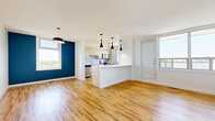 Located at 25 Woodridge Cres in Ottawa's K2B neighbourhood, this 2-bedroom, 1-bathroom unit offers a well-designed layout with modern finishes throughout. The open-concept living and kitchen area serves as the heart of the home, featuring warm hardwood-style flooring, a bold navy accent wall, and large windows that flood the space with natural light and offer outdoor views. Sleek pendant lighting adds a contemporary touch above the kitchen island, which features a clean white countertop and serves as a natural divider between the kitchen and living areas. The kitchen is equipped with light wood cabinetry, a white tile backsplash, stainless steel appliances including a dishwasher, electric range, over-the-range microwave, and refrigerator, along with ample counter and storage space. Both bedrooms carry the same hardwood-style flooring and are finished with soft sage-green accent walls and sliding windows that bring in natural light. The primary bedroom offers a comfortable footprint with a closet and direct hallway access. The bathroom is clean and functional, featuring light tile flooring, a white vanity, and a full soaker tub with tiled surround. Two hallways connect the living areas to the bedrooms and bathroom, contributing to an efficient and practical flow throughout the unit.