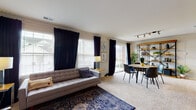 This single-floor residence offers a thoughtfully designed layout that balances comfort and functionality across its key living areas. The open-plan living and dining space is bright and welcoming, with large windows dressed in navy curtains and white blinds that allow generous natural light to fill the room. Soft carpeting runs throughout the living area, complemented by a patterned area rug, while a sliding glass door provides access to an outdoor area. A freestanding shelving unit adds both storage and visual interest to the dining zone, which is anchored by a round table with track lighting overhead. The kitchen features warm wood-trimmed cabinetry with white fronts, light countertops, hardwood-style flooring, and a full suite of appliances including a dishwasher, microwave, and refrigerator, along with a convenient breakfast bar. Both bedrooms are carpeted and well-proportioned, each receiving natural light through large windows with blinds and curtains. The primary bedroom includes ample space for a full dresser and provides access to an adjoining area. The bathroom is clean and simply finished, offering a full soaking tub and shower combination. A dedicated in-unit laundry area with side-by-side washer and dryer units completes this practical and comfortable home.