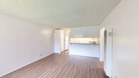 Located at 15363 Goldenwest St in Huntington Beach, California, this one-bedroom, one-bathroom unit offers a well-organized, single-floor layout designed for practical and comfortable living. Throughout the space, wood-look luxury vinyl flooring provides a warm, cohesive aesthetic that ties each room together seamlessly.

The combined kitchen and living area forms the heart of the unit. The kitchen features a peninsula counter with a dark stone-look surface and overhead cabinetry, with an under-cabinet light illuminating the workspace below. A wall-mounted air conditioning unit in the living area ensures year-round climate control, while a front-facing window fills the space with natural light and provides a view to the outdoors. Textured ceilings are present throughout the unit.

The bedroom is a comfortable, well-proportioned room with a horizontal window that draws in natural light. A sliding closet door provides convenient storage, with direct access to the hallway connecting the rest of the unit.

The bathroom is clean and functional, featuring a white vanity with cabinet storage, a toilet, and a full tub-shower combination with chrome fixtures and a shower curtain rod. The consistent wood-look flooring extends into the bathroom, maintaining a unified feel. Overall, this unit offers a tidy, move-in-ready space in a well-located Huntington Beach neighborhood.