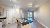 Located at 2700 East McKinney Street in Denton, TX, this one-bedroom, one-bathroom unit offers a well-designed, single-floor layout that maximizes every square foot. The open-concept kitchen and living area serves as the heart of the home, anchored by a central island featuring a double stainless steel sink and striking dark granite countertops. The kitchen is well-appointed with taupe cabinetry, matching dark granite surfaces, and a full suite of stainless steel appliances including a refrigerator, microwave, and range. Track lighting illuminates the kitchen, while a ceiling fan with light kit keeps the living area comfortable. Wood-look flooring runs throughout the main living space, adding warmth and cohesion. French doors in the living room invite natural light and provide a view of the outdoors. The bedroom is a comfortable size, fitted with a ceiling fan, a window with blinds, and the same wood-look flooring. A dedicated closet offers organized storage. The bathroom includes a full soaking tub with a tiled surround in earthy tones. A hallway connects the spaces efficiently, completing this clean, functional, and move-in-ready home.
