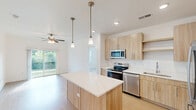 Located at 14801 Statesville Rd in Huntersville, NC, this single-floor, 2-bedroom, 2-bathroom home offers a thoughtfully designed layout with modern finishes throughout. The kitchen serves as a central highlight, featuring light wood cabinetry, stainless steel appliances including a French door refrigerator and electric range, a central island with a white quartz countertop, and warm pendant lighting — all set atop durable light wood flooring that flows seamlessly through the space. Both bathrooms are finished with clean white walls, light wood vanities, quartz countertops, and wood-look flooring; one bathroom includes a full tub-shower combination. The two bedrooms are carpeted and bright, with large windows that invite natural light and ceiling fans for added comfort. The primary bedroom is generously sized and connects conveniently to the kitchen area. Each bedroom is accompanied by a dedicated walk-in closet outfitted with wire shelving systems, providing practical storage solutions. The overall design aesthetic is clean and contemporary, with a neutral color palette of whites and warm wood tones creating a cohesive, inviting atmosphere throughout the home.