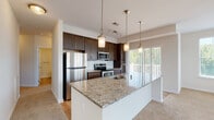 This single-floor residence is designed with a cohesive contemporary aesthetic, blending functional layouts with upscale finishes throughout. The kitchen serves as a central highlight, showcasing rich dark espresso cabinetry that extends to the ceiling for abundant storage, paired with a classic white subway tile backsplash and stainless steel appliances including a refrigerator, range, and microwave. A large granite-topped island with an undermount sink provides generous prep space and casual seating, while pendant lighting and a track light system enhance the workspace. Natural light flows in through a sliding glass door nearby.

The bedrooms are carpeted and generously proportioned, each benefiting from wide windows that frame outdoor views of surrounding greenery. One bedroom features dual closets, while another offers a spacious walk-in closet outfitted with wire shelving for organized storage. The en suite bathroom is finished with the same dark cabinetry and granite countertop as the kitchen, complemented by a double-sink vanity, wood-look flooring, and a glass-enclosed walk-in shower with subway tile surround.

A dedicated laundry area with a full-size washer and dryer adds everyday convenience, completing this well-appointed and thoughtfully designed residence.